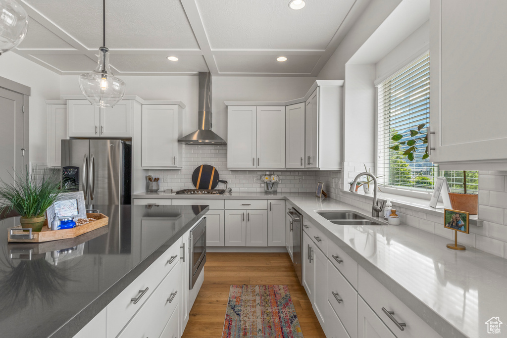Kitchen with appliances with stainless steel finishes, a sink, wall chimney range hood, recessed lighting, and light wood-style flooring