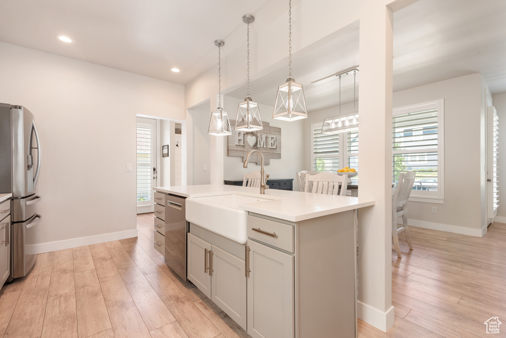 Kitchen with appliances with stainless steel finishes, a sink, light wood-style floors, light countertops, and decorative light fixtures