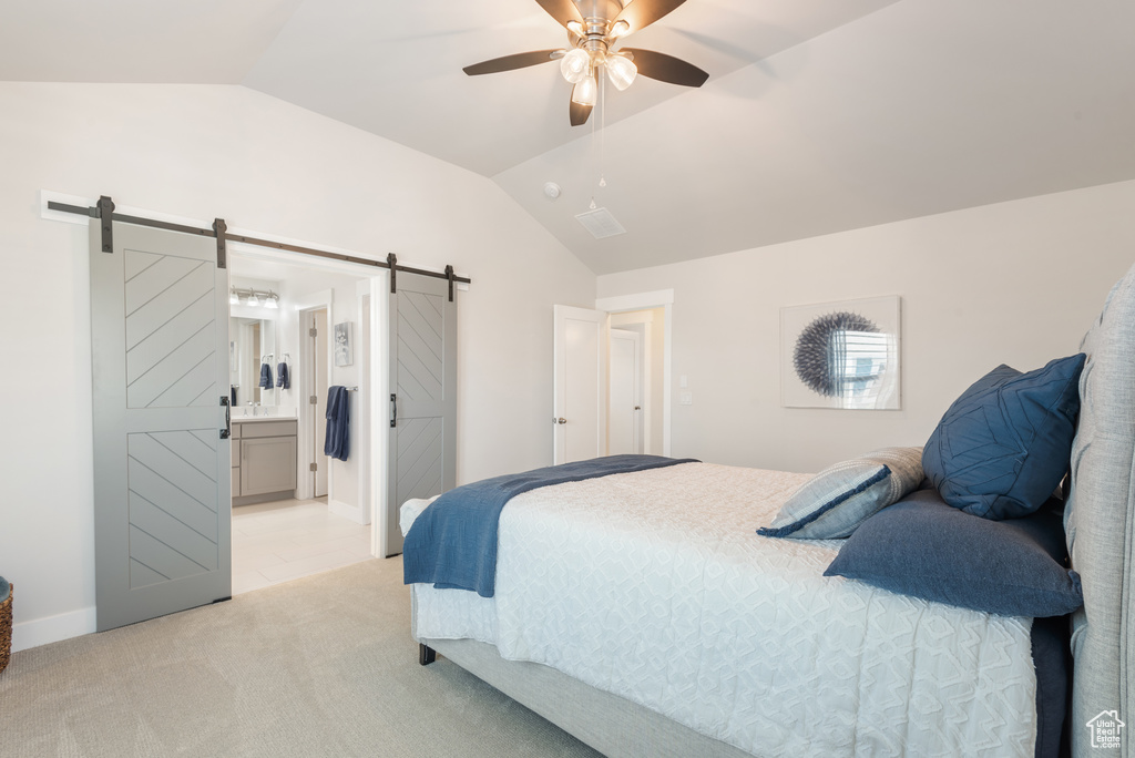 Bedroom with a barn door, vaulted ceiling, light carpet, connected bathroom, and a ceiling fan