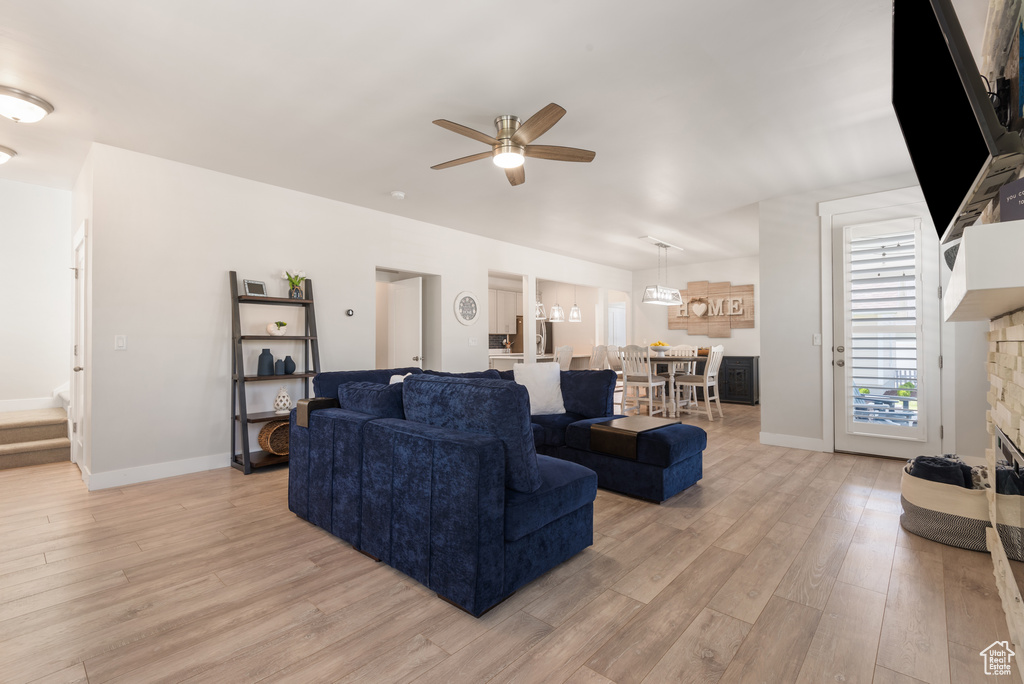 Living room featuring light wood-style flooring, a ceiling fan, and baseboards