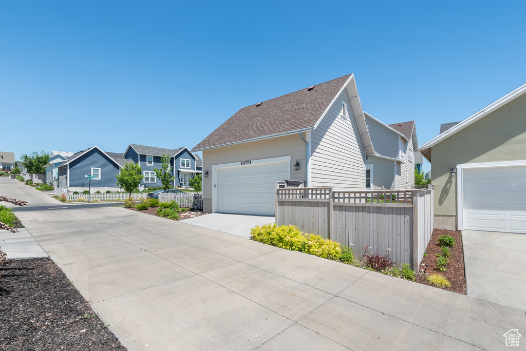 View of property exterior with a residential view, concrete driveway, and a shingled roof