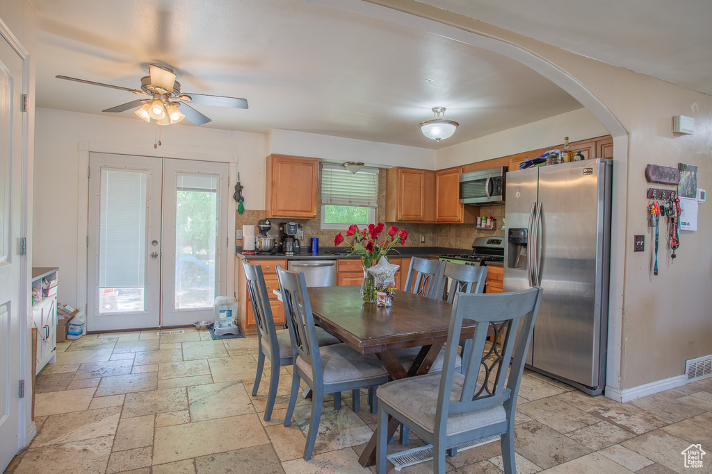 Dining area featuring stone tile flooring, arched walkways, ceiling fan, and french doors