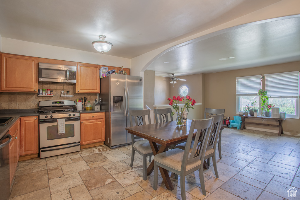 Kitchen with appliances with stainless steel finishes, stone tile flooring, a ceiling fan, dark countertops, and tasteful backsplash
