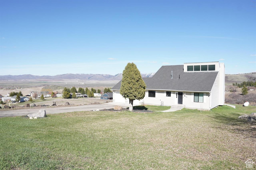 Rear view of house featuring a yard, a mountain view, and roof with shingles