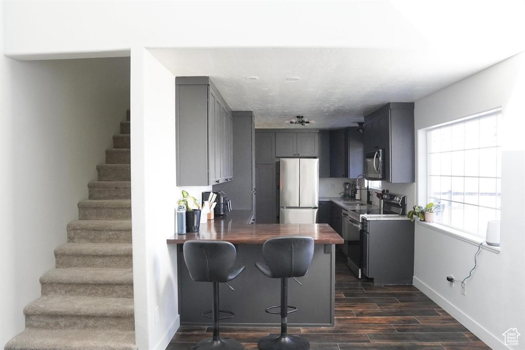 Kitchen featuring appliances with stainless steel finishes, gray cabinets, dark wood-style floors, baseboards, and a peninsula