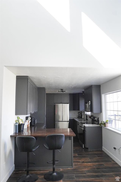 Kitchen featuring appliances with stainless steel finishes, a peninsula, a kitchen bar, dark wood finished floors, and baseboards