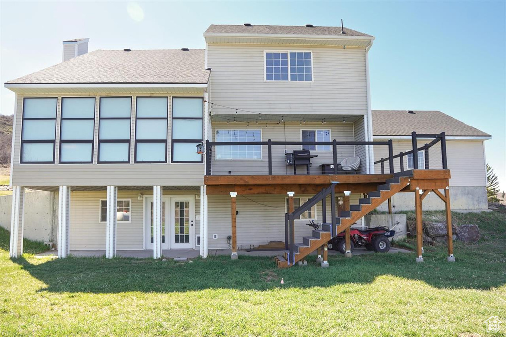 Rear view of property with stairway, a wooden deck, a lawn, and roof with shingles