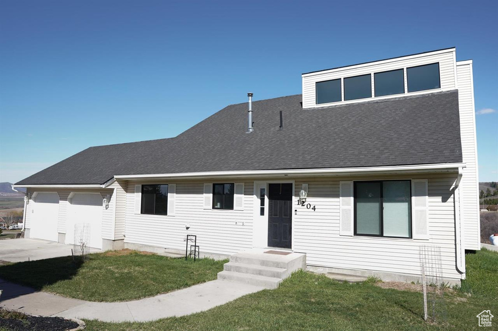 View of front facade with a front yard, driveway, an attached garage, and roof with shingles