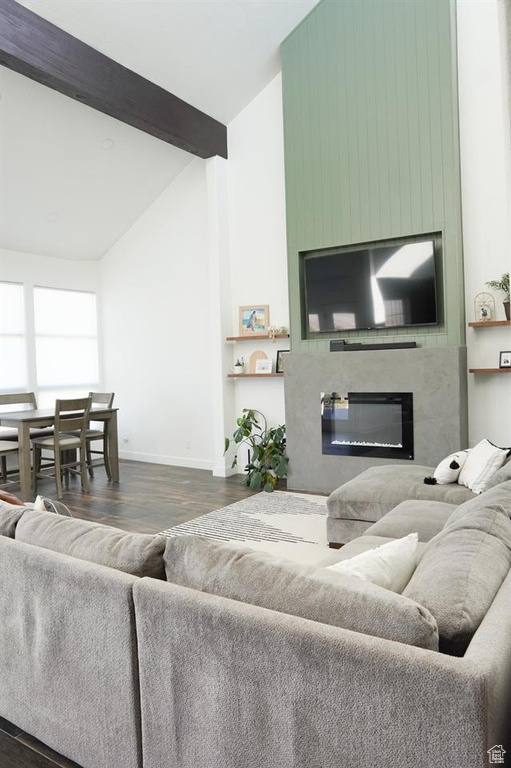 Living area featuring dark wood-type flooring, a large fireplace, high vaulted ceiling, baseboards, and beamed ceiling