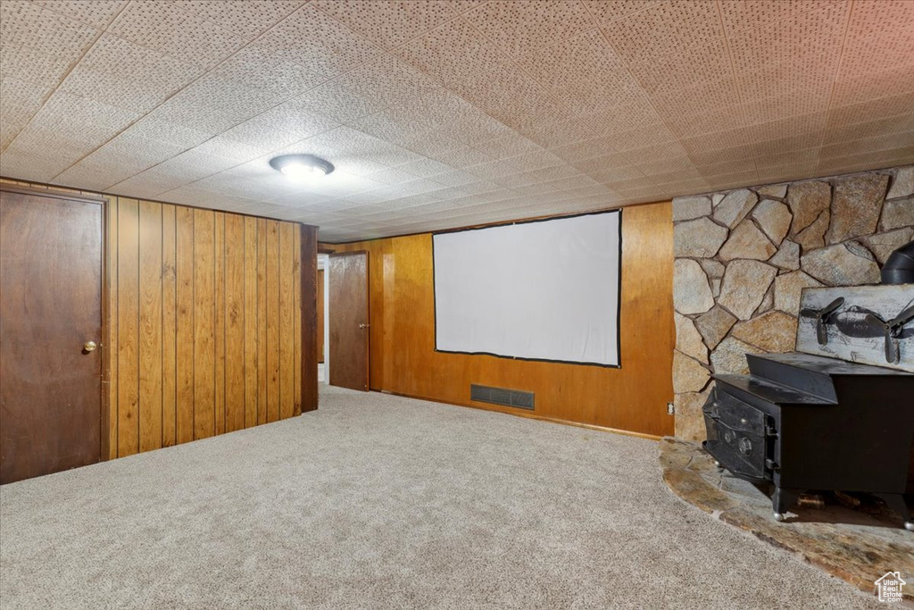 Home theater room with carpet flooring, a wood stove, and wooden walls