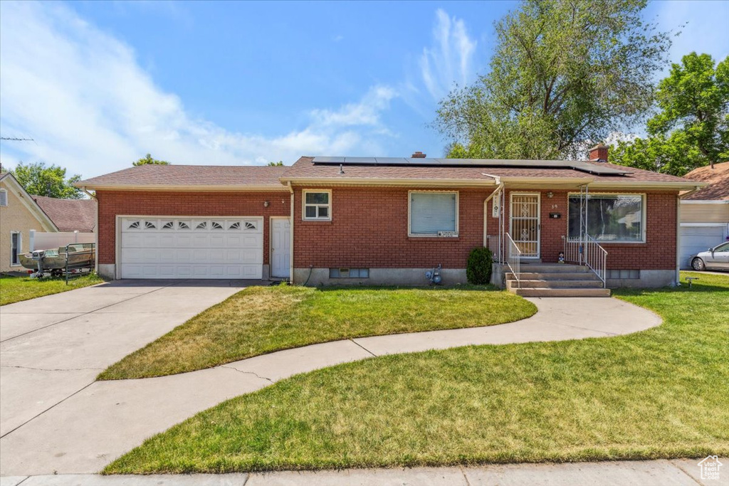 Ranch-style home with a garage, brick siding, driveway, and roof mounted solar panels
