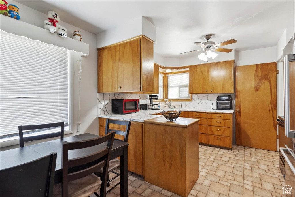 Kitchen featuring a peninsula, backsplash, a ceiling fan, and brown cabinets