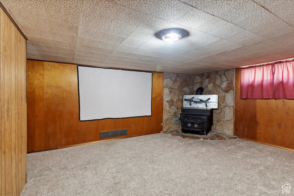 Home theater featuring a wood stove, wooden walls, and carpet floors