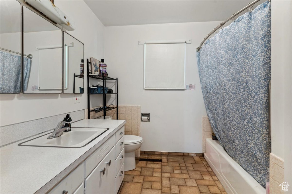 Full bathroom featuring vanity, toilet, shower / bath combo, baseboards, and stone finish floors