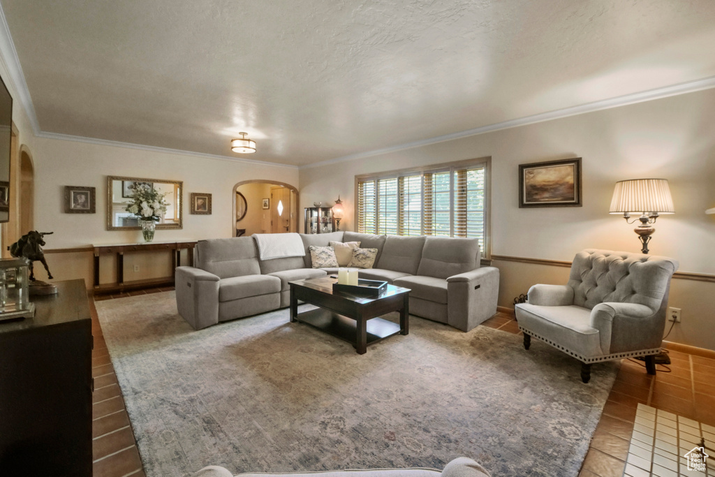 Living room featuring arched walkways, ornamental molding, baseboards, tile patterned floors, and a textured ceiling