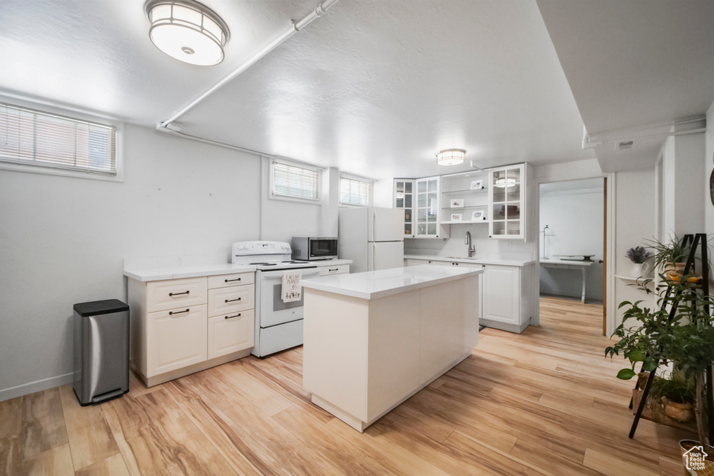 Kitchen featuring white appliances, a sink, white cabinets, a center island, and light wood-style flooring
