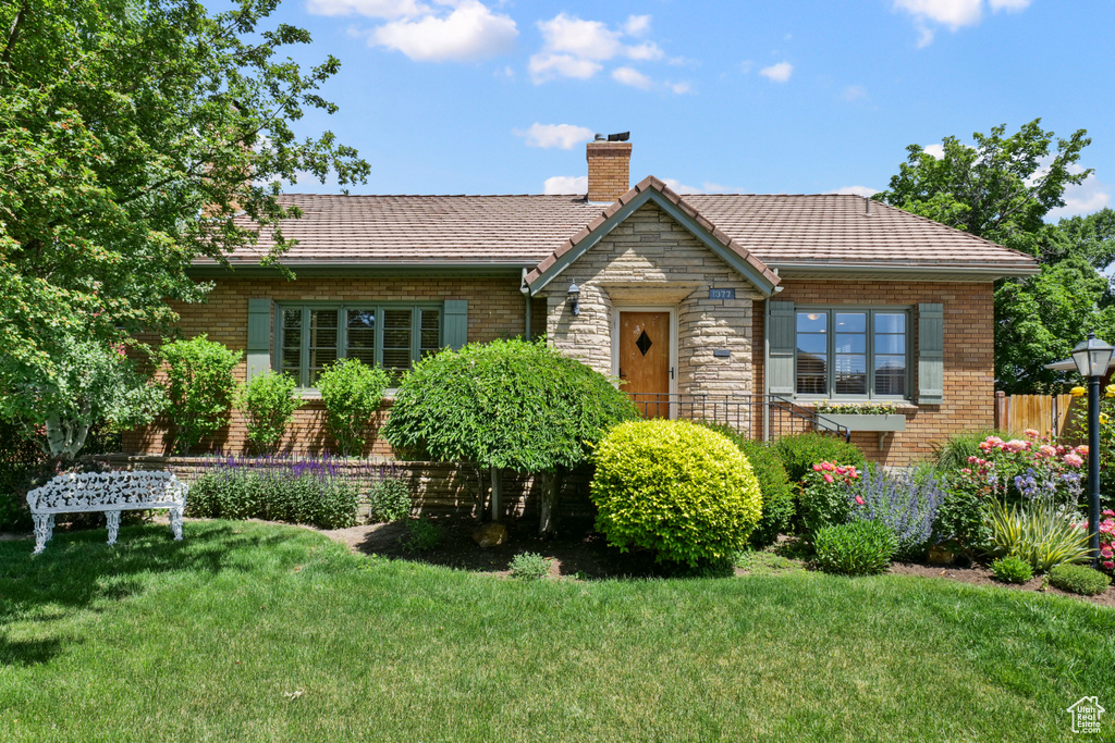 View of front of home with a front yard, a chimney, brick siding, and stone siding