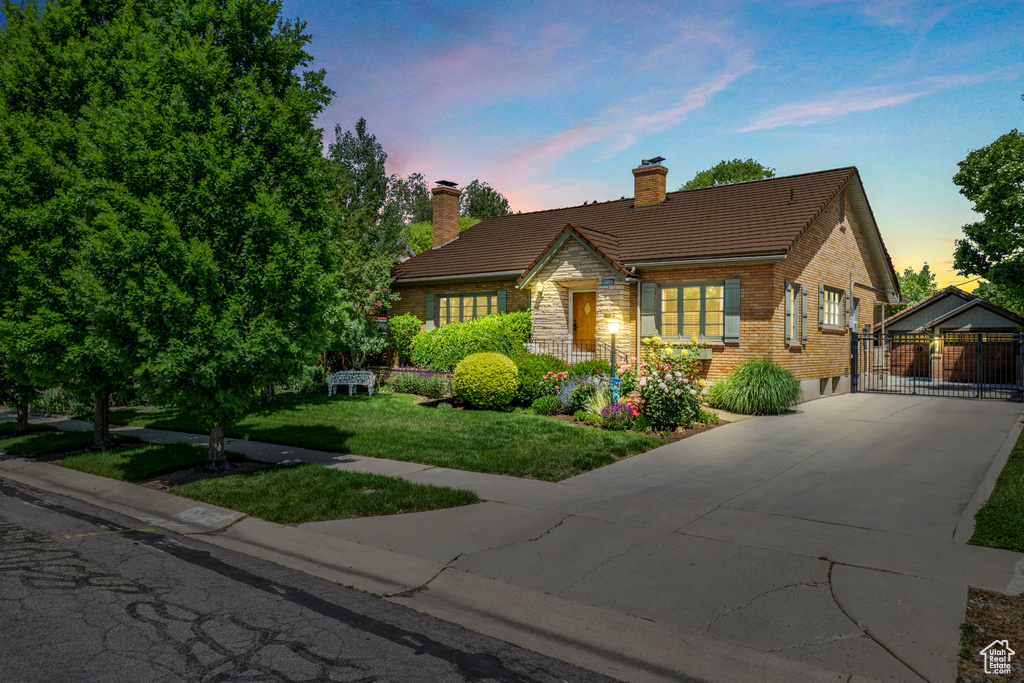 View of front of property featuring driveway, a chimney, brick siding, and a yard
