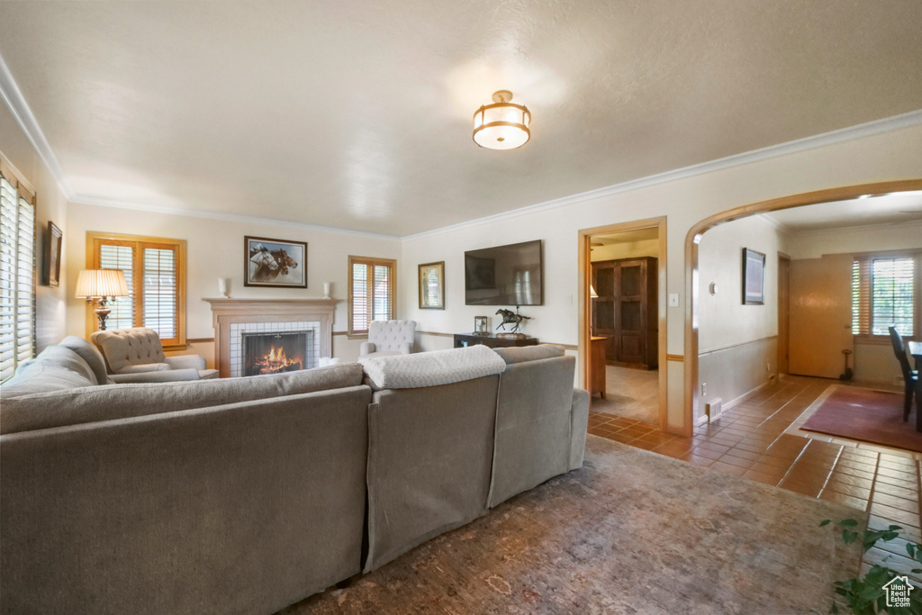 Living room featuring arched walkways, tile patterned flooring, ornamental molding, and a brick fireplace