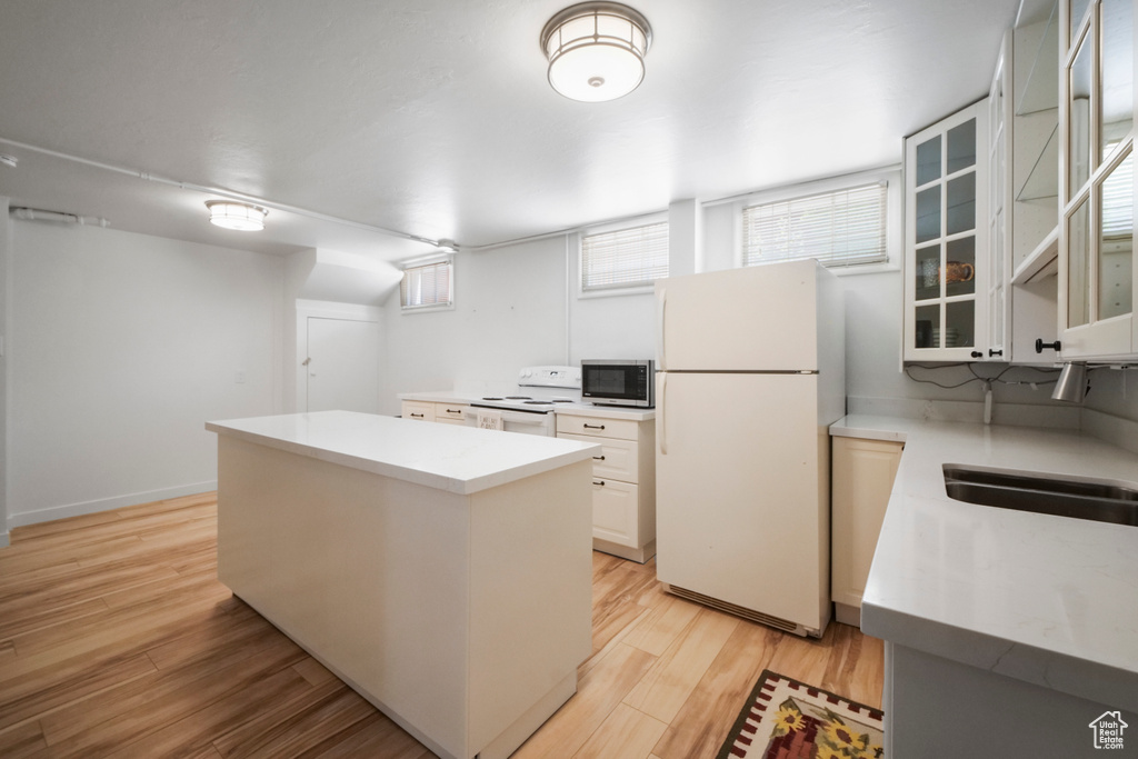 Kitchen with white appliances, a kitchen island, light countertops, glass insert cabinets, and light wood-type flooring
