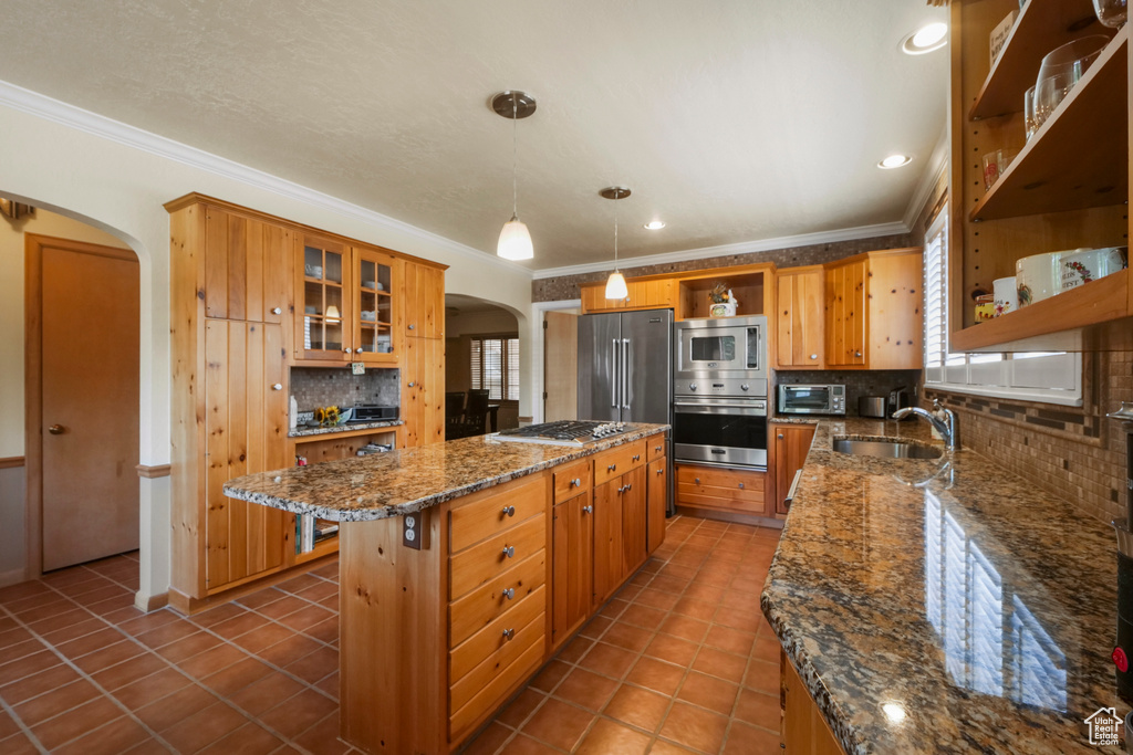 Kitchen featuring open shelves, stainless steel appliances, arched walkways, a sink, and a center island