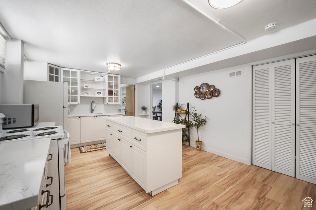 Kitchen with stainless steel microwave, a sink, white range with electric cooktop, light wood-style flooring, and white cabinetry