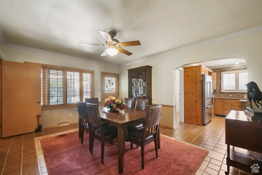 Dining room featuring arched walkways, light tile patterned floors, ornamental molding, ceiling fan, and baseboards