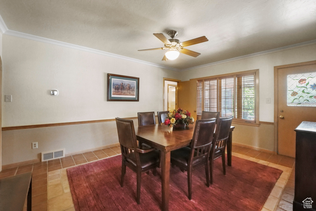Tiled dining space with ceiling fan and crown molding