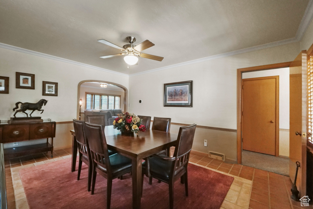 Tiled dining space with arched walkways, crown molding, and ceiling fan