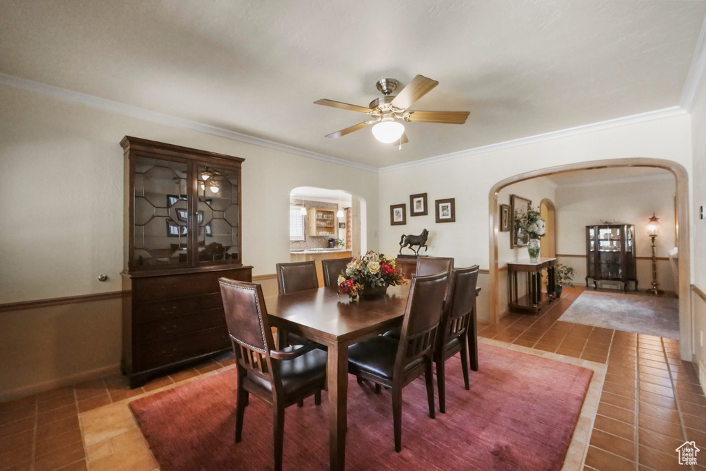 Dining area featuring arched walkways, tile patterned flooring, a ceiling fan, crown molding, and baseboards