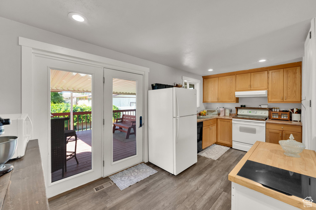 Kitchen with white appliances, under cabinet range hood, wood finished floors, light countertops, and recessed lighting