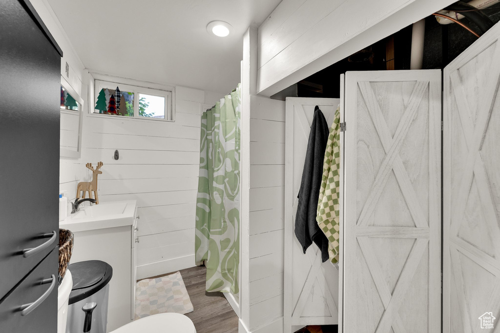 Bathroom with wood finished floors, vanity, toilet, a shower with curtain, and wooden walls
