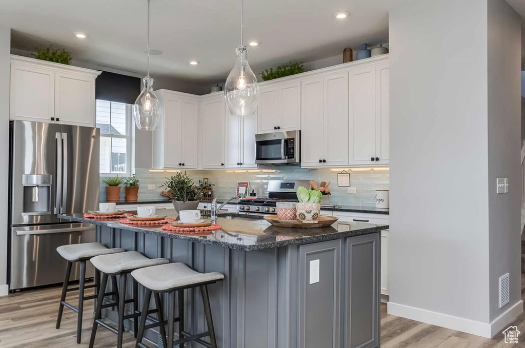 Kitchen with stainless steel appliances, light wood-style flooring, backsplash, a breakfast bar, and a sink