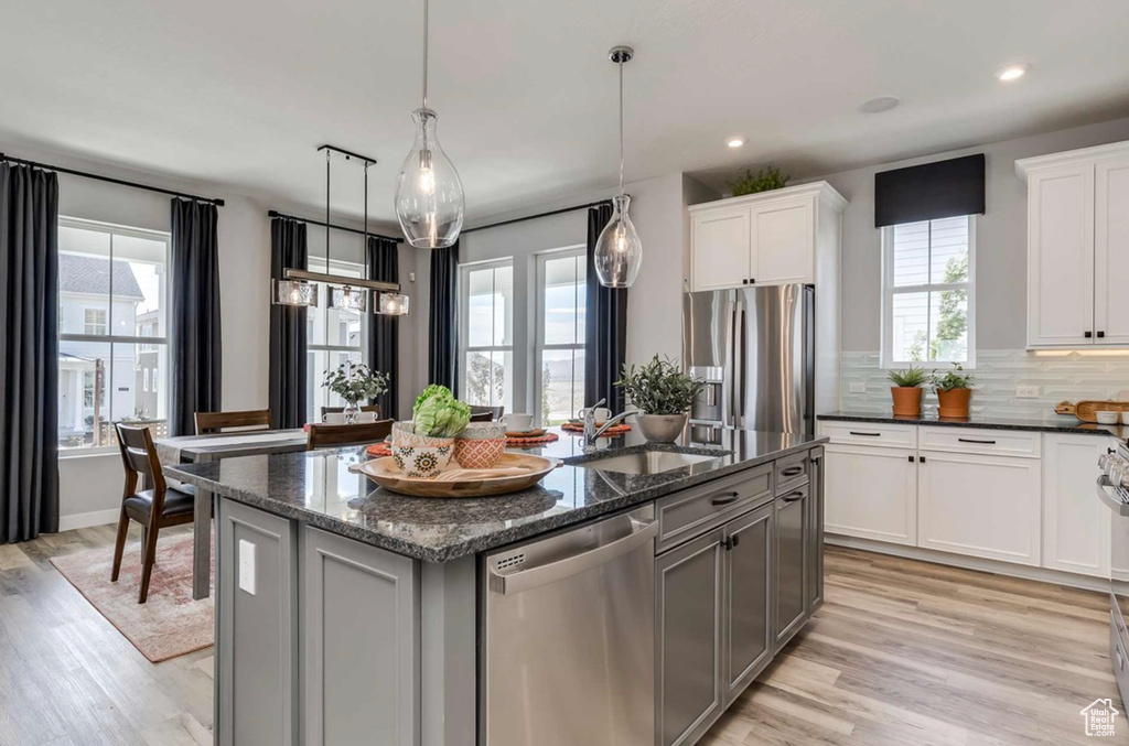 Kitchen featuring appliances with stainless steel finishes, a sink, a kitchen island with sink, light wood finished floors, and dark stone countertops