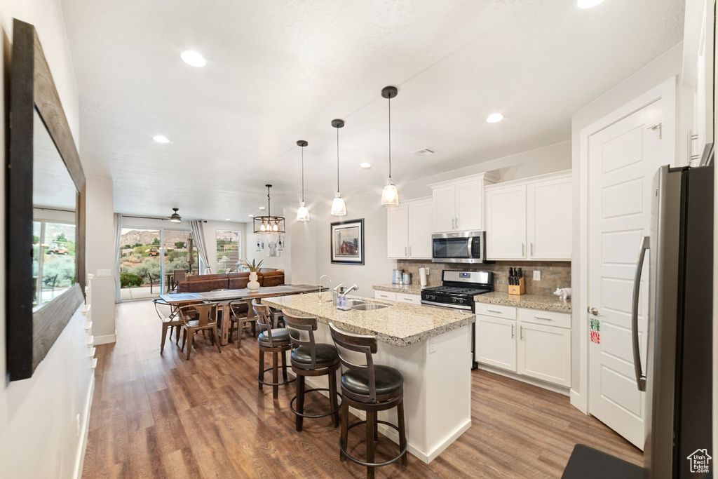 Kitchen with stainless steel appliances, wood finished floors, decorative backsplash, white cabinets, and recessed lighting