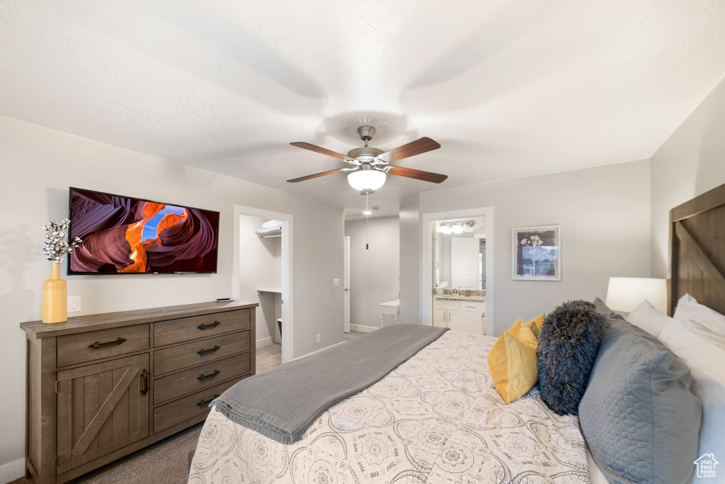 Carpeted bedroom with a spacious closet, ensuite bathroom, baseboards, and ceiling fan