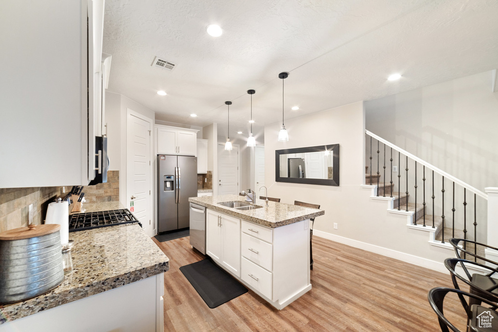 Kitchen featuring stainless steel appliances, a sink, light wood-type flooring, backsplash, and white cabinetry