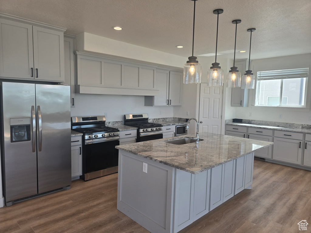Kitchen with appliances with stainless steel finishes, a sink, dark wood-style floors, a textured ceiling, and a kitchen island with sink