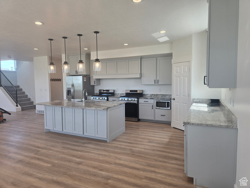 Kitchen with stainless steel appliances, light wood-style floors, recessed lighting, light stone countertops, and gray cabinetry