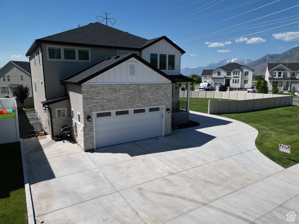 View of property exterior featuring stone siding, driveway, a mountain view, a shingled roof, and a residential view