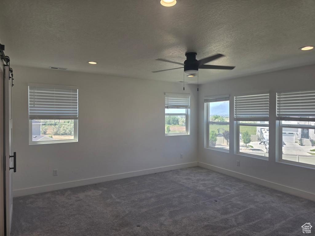 Spare room featuring dark colored carpet, a textured ceiling, a barn door, baseboards, and ceiling fan
