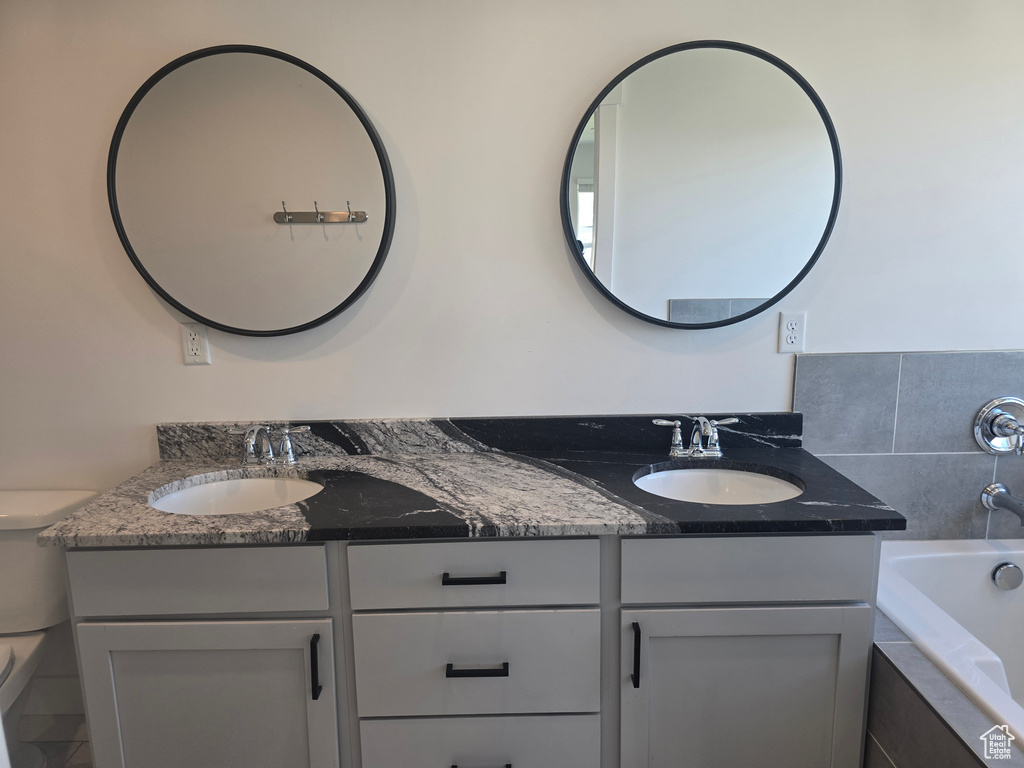 Full bath with double vanity, toilet, and tiled tub