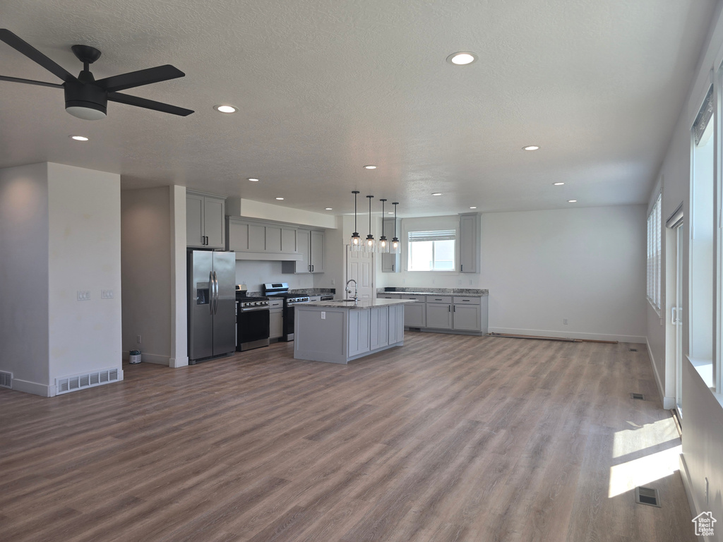 Kitchen featuring stainless steel refrigerator with ice dispenser, gray cabinetry, open floor plan, a sink, and ceiling fan