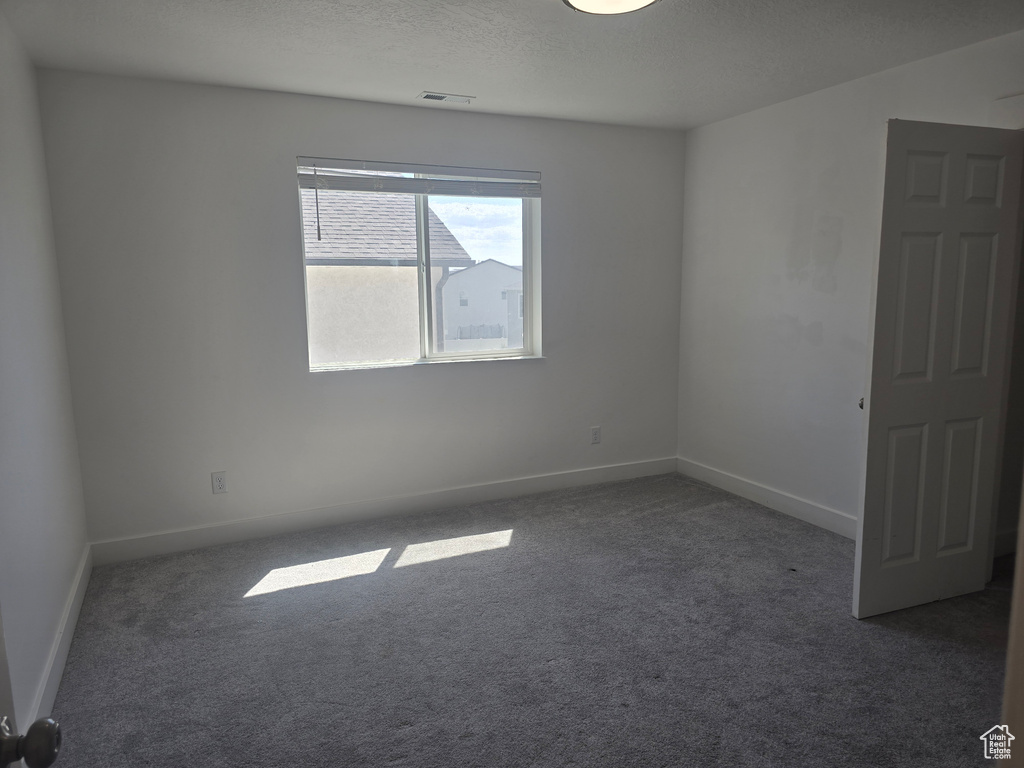 Unfurnished room featuring dark colored carpet, baseboards, and a textured ceiling