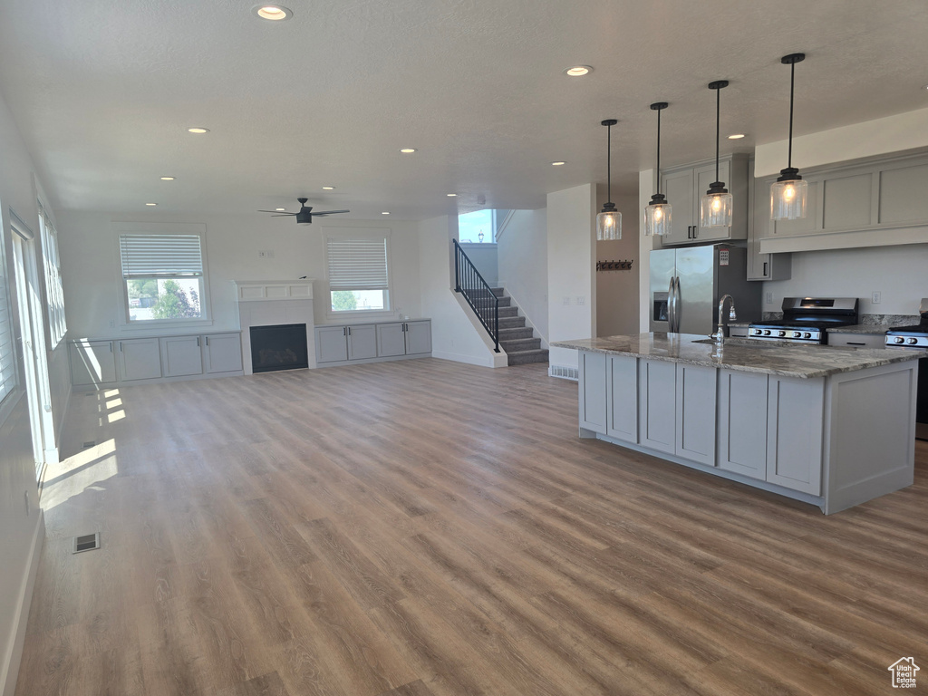 Kitchen featuring appliances with stainless steel finishes, wood finished floors, ceiling fan, recessed lighting, and an island with sink
