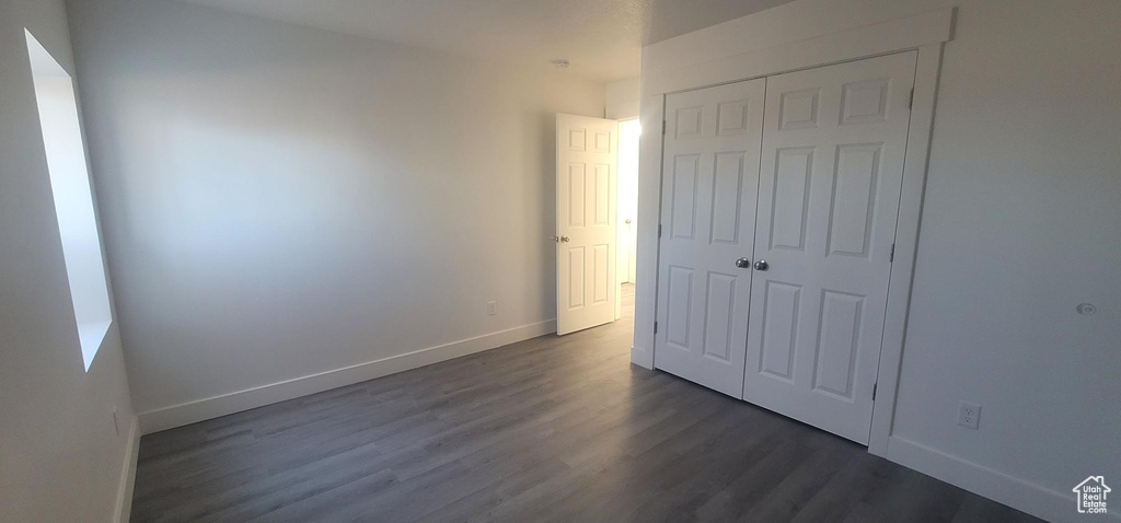 Unfurnished bedroom featuring a closet, baseboards, and dark wood-style floors