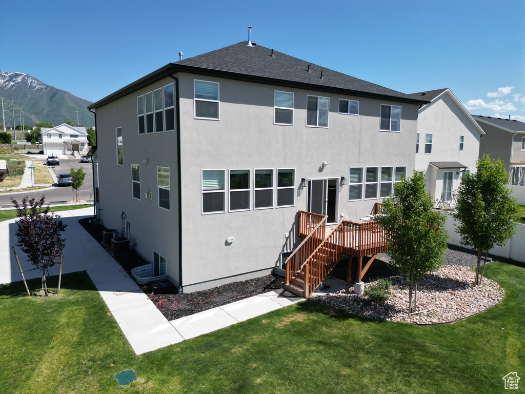 Rear view of house with stucco siding, a deck with mountain view, and a yard