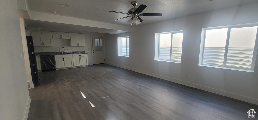Unfurnished living room featuring baseboards, ceiling fan, dark wood-style floors, and a sink