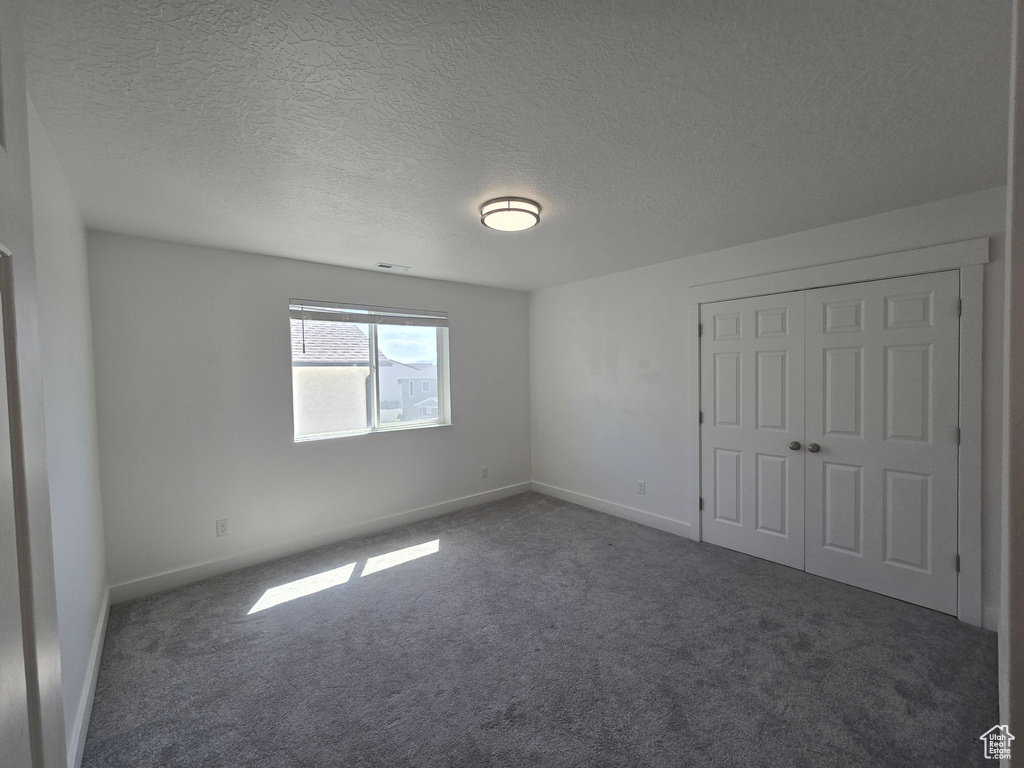 Unfurnished bedroom with carpet floors, baseboards, a textured ceiling, and a closet