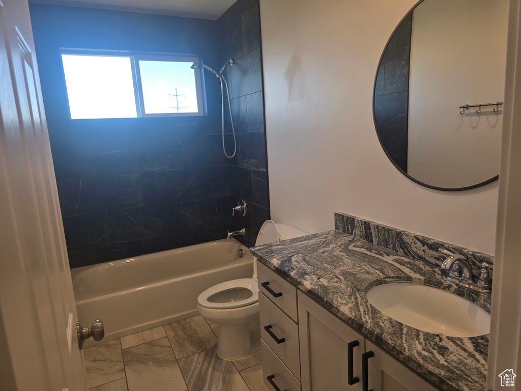 Full bath featuring toilet,  shower combination, vanity, and marble look tiles